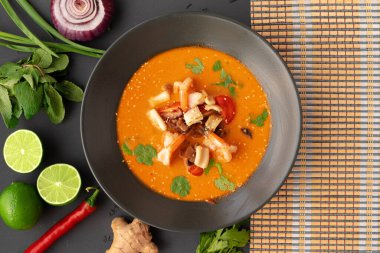 Tom yam Thai çorbası, gri arka planda servis edilir.