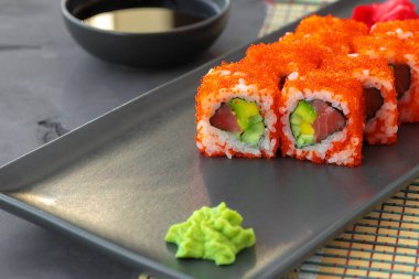 Kaliforniya suşi rulosu siyah seramik tabakta servis edilir.