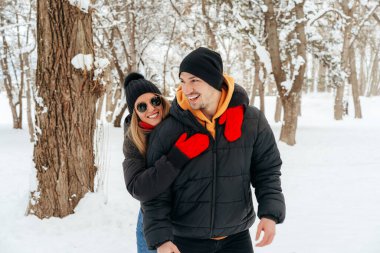 Mutlu çift dışarıda karlı parkta sarılıp gülümsüyor.