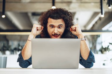 Heyecanlı genç iş adamı dizüstü bilgisayara bakıyor. Kazanmaktan mutlu ya da iyi haberler alıyor.