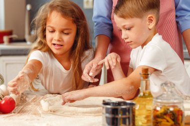Çocuklarıyla mutfakta hamur yoğuran bir kadın.