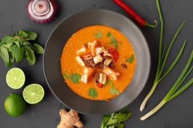 Tom yam Thai çorbası, gri arka planda servis edilir.