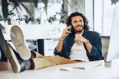 Ofiste cep telefonu kullanan sıradan giyinmiş genç bir iş adamı.