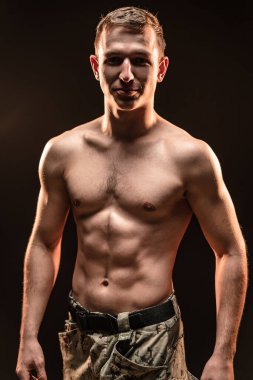 Siyah arka plandaki kaslı üstsüz askerin stüdyo fotoğrafı.