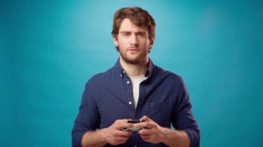 Genç sakallı adam mavi arka planda joystick konsoluyla bilgisayar oyunu oynuyor