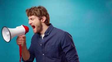 Sinirli sakallı genç adam mavi arka planda megafonla bağırıyor.