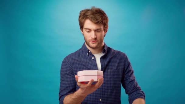 Mladý ležérní vousatý muž otevření lepenkové krabice na modrém pozadí — Stock video