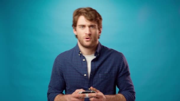 Jovem barbudo joga jogo pc com joystick console contra fundo azul — Vídeo de Stock