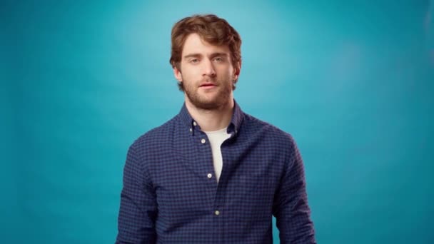 Jongeman in blauw shirt met een beetje gebaar, klein formaat tegen blauwe achtergrond — Stockvideo