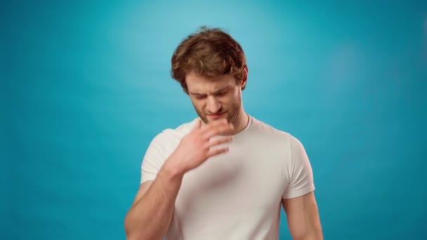Tired young man rubbing his eyes, portrait against blue background — Stock Video