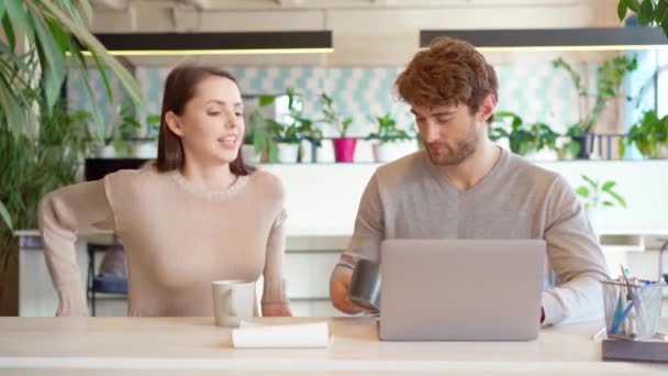 Jovem homem casual trabalhando no laptop no escritório, colega do sexo feminino traz-lhe bebida em uma xícara, eles discutem projeto juntos — Vídeo de Stock