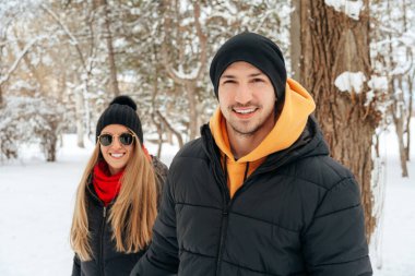 Mutlu çift dışarıda karlı parkta sarılıp gülümsüyor.