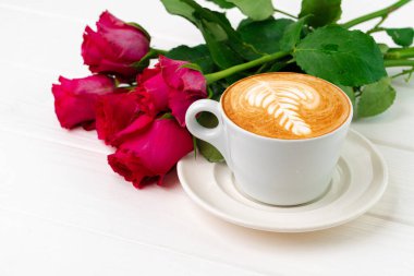 Bir bardak kapuçino ve ahşap masada bir buket gül.