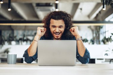 Heyecanlı genç iş adamı dizüstü bilgisayara bakıyor. Kazanmaktan mutlu ya da iyi haberler alıyor.