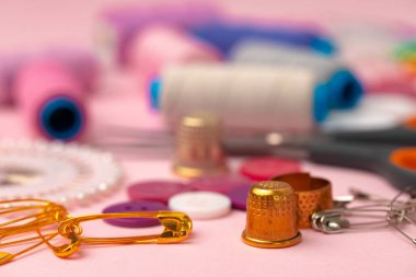 Pembe arka planda iplik makaraları ve iğneler de dahil olmak üzere aksesuarlar dikiliyor