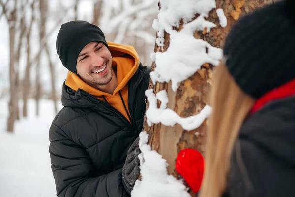 Young loving couple play hide and seek in a snowy winter park — Stock Photo, Image