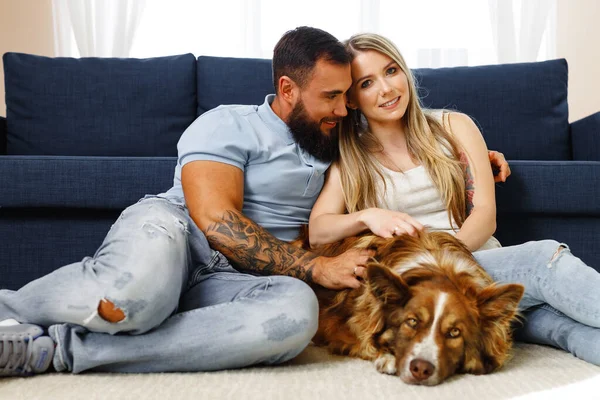 Joven pareja amante relajarse en la sala de estar con su mascota perro — Foto de Stock