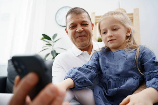 할아버지와 어린 손녀 가집에서 스마트폰으로 무엇인가를보고 있는 모습 — 스톡 사진