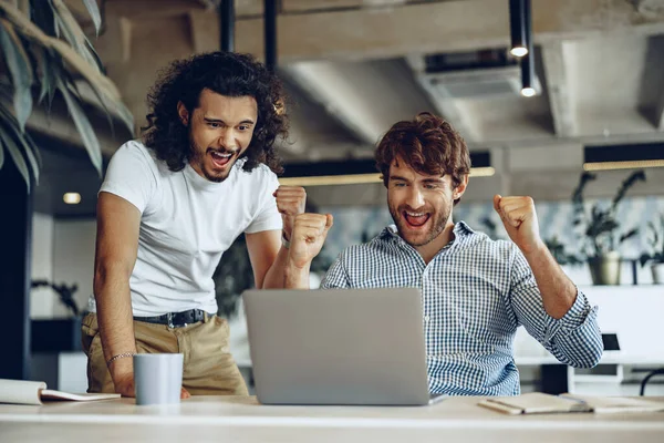 Zwei aufgeregte, überglückliche junge Geschäftsleute schauen auf den Laptop-Bildschirm und freuen sich über den Gewinn oder die gute Nachricht — Stockfoto