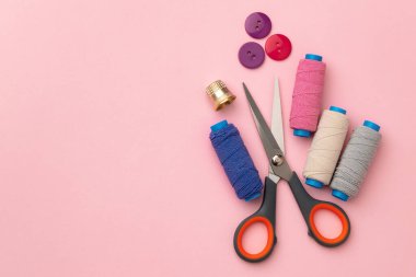 Pembe arka planda çok renkli iplik makaraları ve düğmeleri