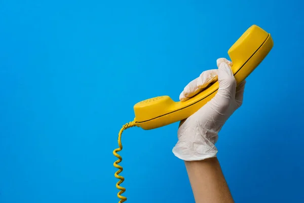 Mano femminile in guanto medico con altoparlante telefonico giallo — Foto Stock