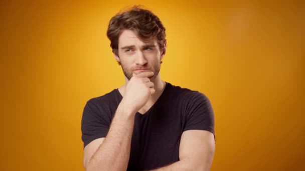 Nachdenklicher junger Mann überlegt etwas, berührt sein Kinn, gelber Hintergrund — Stockvideo