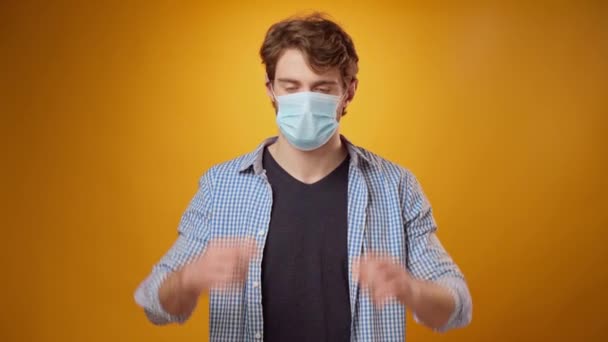 Young man takes off his medical face mask against yellow studio background — Stock Video