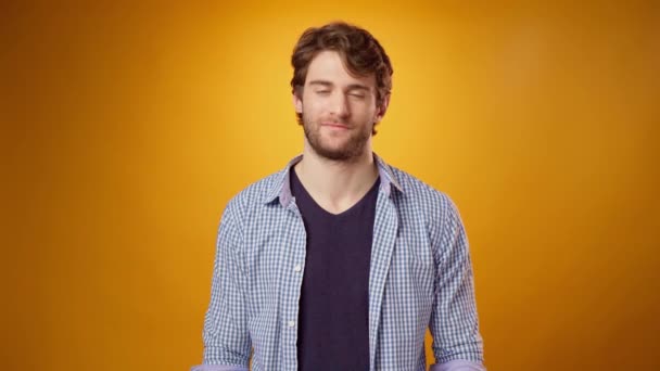 Young beared guy in casual shirt nods approvingly against yellow studio background — Stock Video