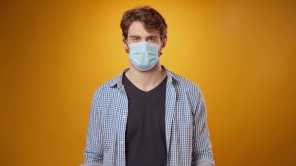 Young man takes off his medical face mask against yellow studio background — Stock Video