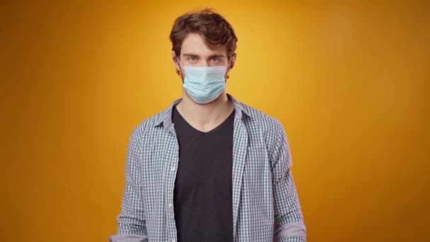 Mladý muž v lékařských maskách gesta "Já nevím" na žlutém pozadí — Stock video