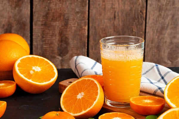 Vaso de jugo de naranja y naranjas cortadas en la mesa — Foto de Stock