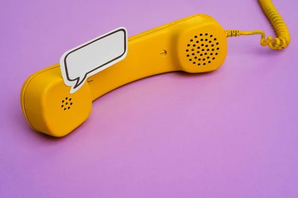 Telefone fixo amarelo com bolha de fala no fundo roxo — Fotografia de Stock