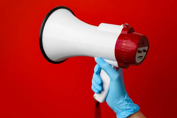 Mano humana en guante médico sosteniendo megáfono electrónico sobre fondo rojo — Foto de Stock