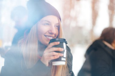 Şapkalı kadın bardağın arkasında kahvesini yudumluyor.