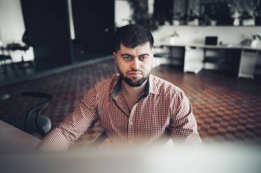 Gündelik gömlekli genç adam ofiste bilgisayarla çalışıyor.