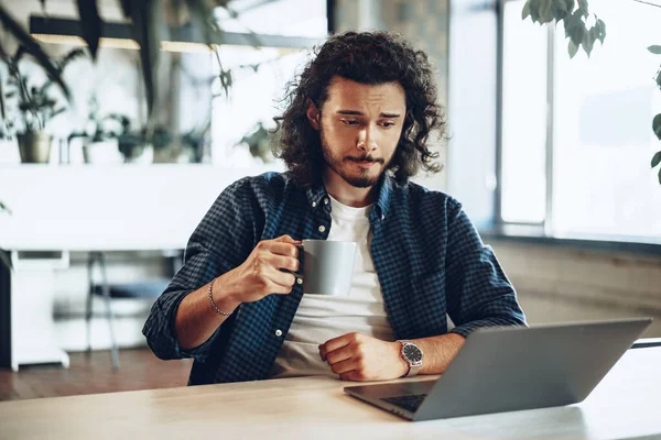 Ung affärsman använder laptop och håller en kopp kaffe på kontoret — Stockfoto