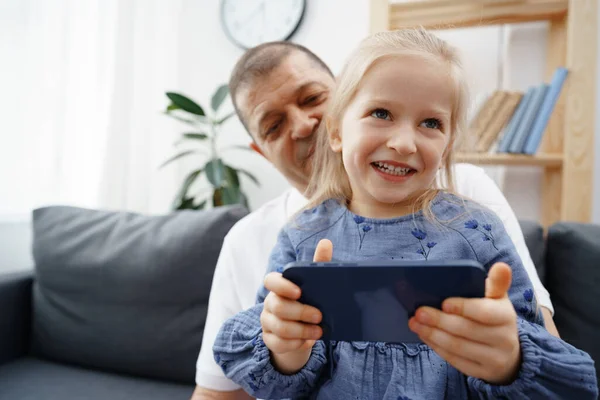 Abuelo y nieta pequeña viendo algo en el teléfono inteligente en casa — Foto de Stock
