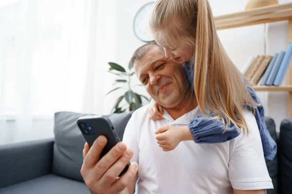 Abuelo y nieta pequeña viendo algo en el teléfono inteligente en casa — Foto de Stock