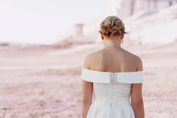 Vista posterior de una novia en un vestido blanco con hombros desnudos de pie en un campo — Foto de Stock