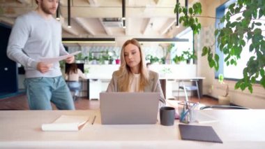 Genç ve güzel iş kadını resmi giysiler giyip ofiste dizüstü bilgisayarla çalışırken erkek arkadaşı belgelerini getiriyor.