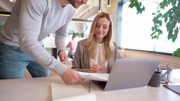 Young beautiful businesswoman wearing formal clothes working on laptop in office while her male colleague brings her documents — Stock Video