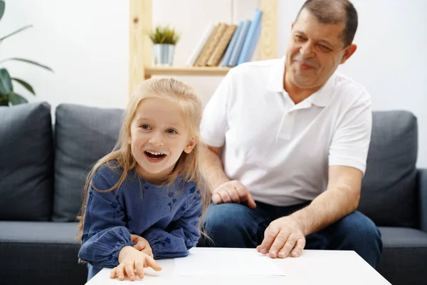 Grandpa and little granddaughter sitting on sofa at home — Stock Photo, Image