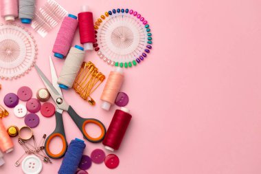 Pembe arka planda iplik makaraları ve iğneler de dahil olmak üzere aksesuarlar dikiliyor