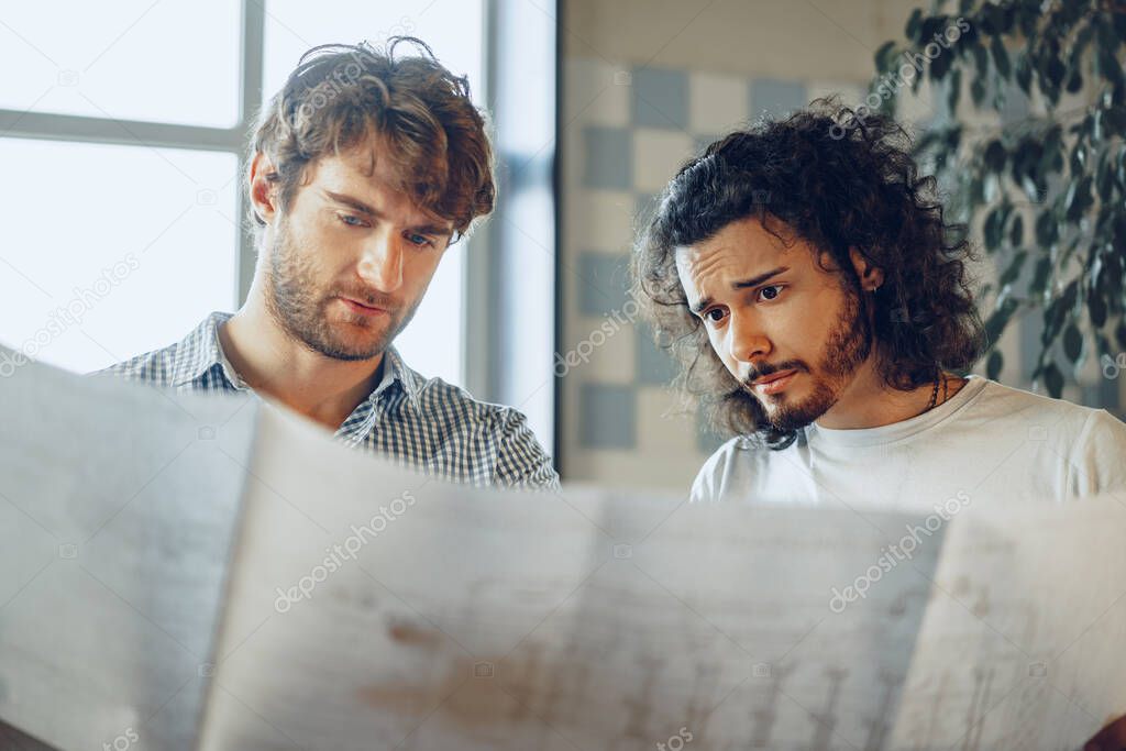 Two young businessmen looking at blueprint and discussing it