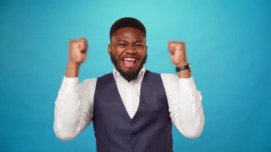 Neşeli, mutlu, Afro-Amerikalı genç adam başarıyı kutluyor, kazanan o, mavi arka plan.