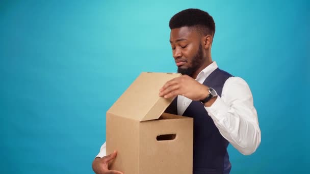 年轻的非洲男人打开纸盒，不喜欢蓝色背景的盒子里有什么？ — 图库视频影像