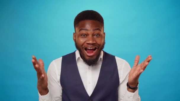 Překvapený mladý africký muž ukazuje palce nahoru proti modrému pozadí ve studiu — Stock video