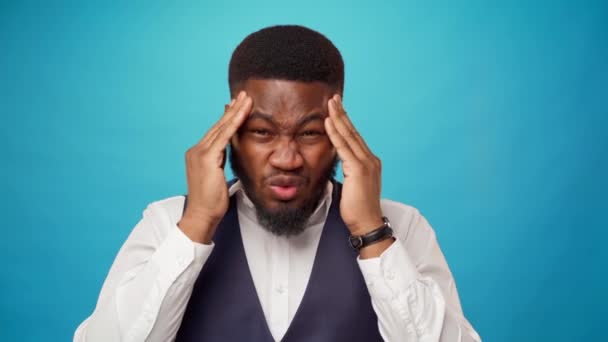 Young african man suffering from headache massaging his forehead, blue background — Stock Video