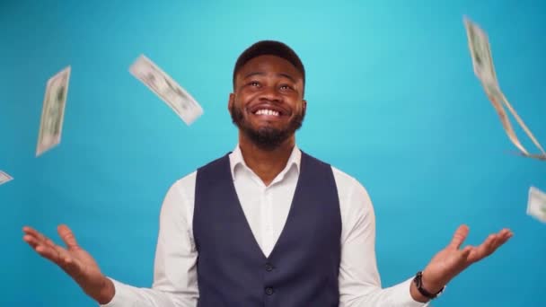 Hombre de negocios afroamericano de pie entre los billetes en dólares caídos sobre fondo azul — Vídeos de Stock