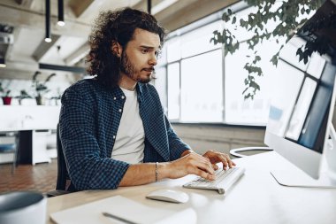 Genç işadamı, başarılı bir serbest çalışan bilgisayar üzerinde çalışıyor, modern ofiste oturuyor.